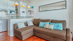 Un espacio habitable moderno con un sofá seccional marrón, una isla de cocina con encimera de vidrio, armarios blancos y un espejo grande en la pared.