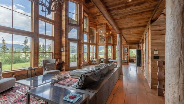 A spacious room with large windows, a wooden ceiling, a sofa, a table, and a view of the outdoors. - Sleeps 23, 8 BR w/ full bath, majestic views on 35 acres, walk to town (Crested Butte)