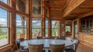 A wooden interior with large windows, a round dining table, and leather chairs. - Sleeps 23, 8 BR w/ full bath, majestic views on 35 acres, walk to town (Crested Butte)