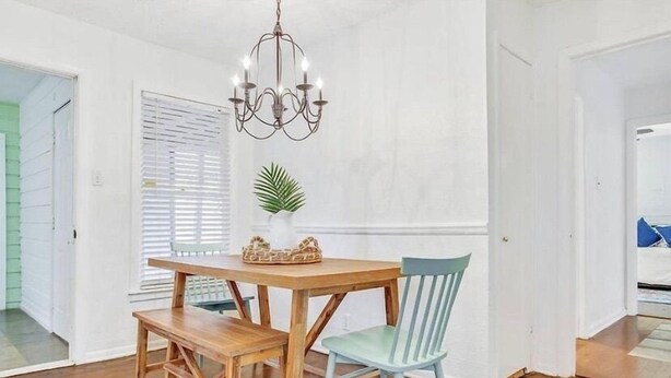 A dining area with a wooden table and bench, a light blue chair, a chandelier, and a potted plant. - 3 BR Walking Distance to ATT, Globe Life & Entertainment District (Arlington)