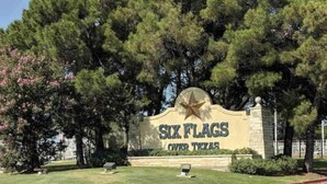 A sign for 'Six Flags Over Texas' with a star emblem, surrounded by trees and grass. - 3 BR Walking Distance to ATT, Globe Life & Entertainment District (Arlington)
