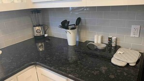 A kitchen with a black countertop, white cabinets, a coffee maker, a kettle, and some condiments. - 3 BR Walking Distance to ATT, Globe Life & Entertainment District (Arlington)