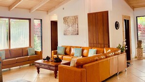 A spacious living room with a high ceiling and wooden beams, featuring a large sofa set and a coffee table. - Poipu Beach Estates: Walk to Beach/Shops, Sleeps 8-16, AC, Pool, Fitness Club! (Koloa)