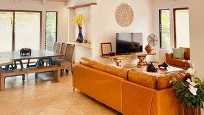 A spacious living room with a high ceiling, a large sofa, a dining table, and a TV. - Poipu Beach Estates: Walk to Beach/Shops, Sleeps 8-16, AC, Pool, Fitness Club! (Koloa)
