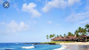 A beachfront hotel with a large building, palm trees, and ocean waves. - Poipu Beach Estates: Walk to Beach/Shops, Sleeps 8-16, AC, Pool, Fitness Club! (Koloa)