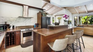 A modern kitchen with a central island, stainless steel appliances, and a high ceiling with exposed beams. - Poipu Beach Estates: Walk to Beach/Shops, Sleeps 8-16, AC, Pool, Fitness Club! (Koloa)