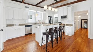 A spacious kitchen with white cabinets, a central island with bar stools, and wooden beams on the ceiling.