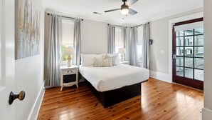 A bedroom with a bed, nightstands, a ceiling fan, and a large window with curtains.