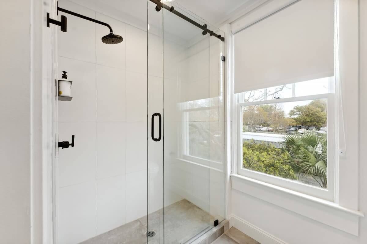A glass-enclosed shower with a handheld showerhead, a soap dispenser, and a control panel.
