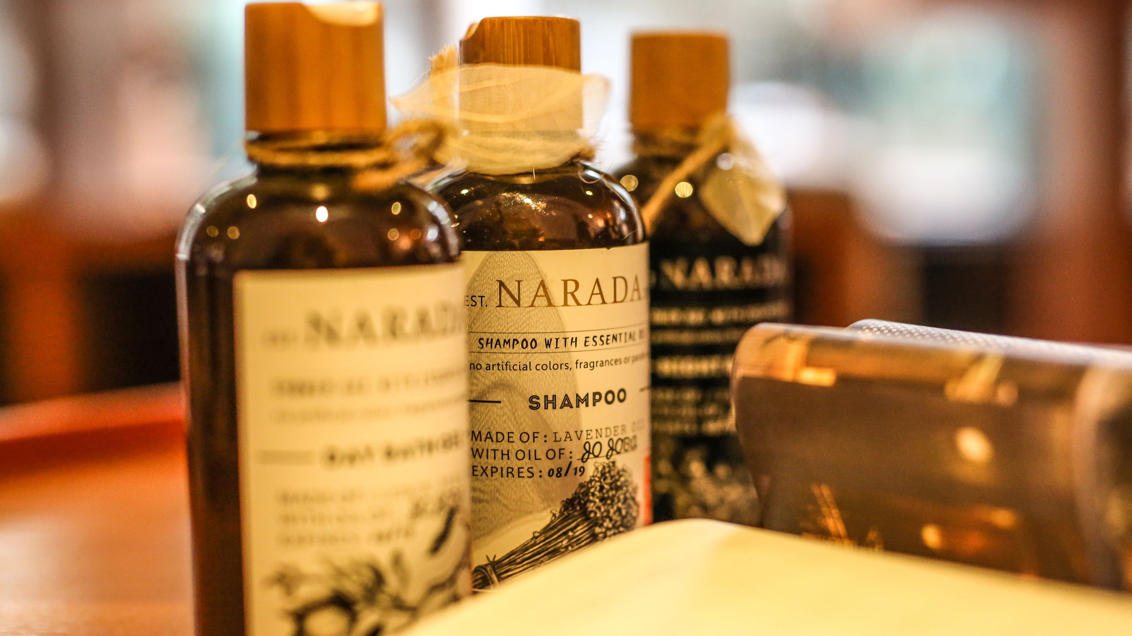 Três frascos de shampoo Narada com óleos essenciais, sobre uma superfície de madeira.