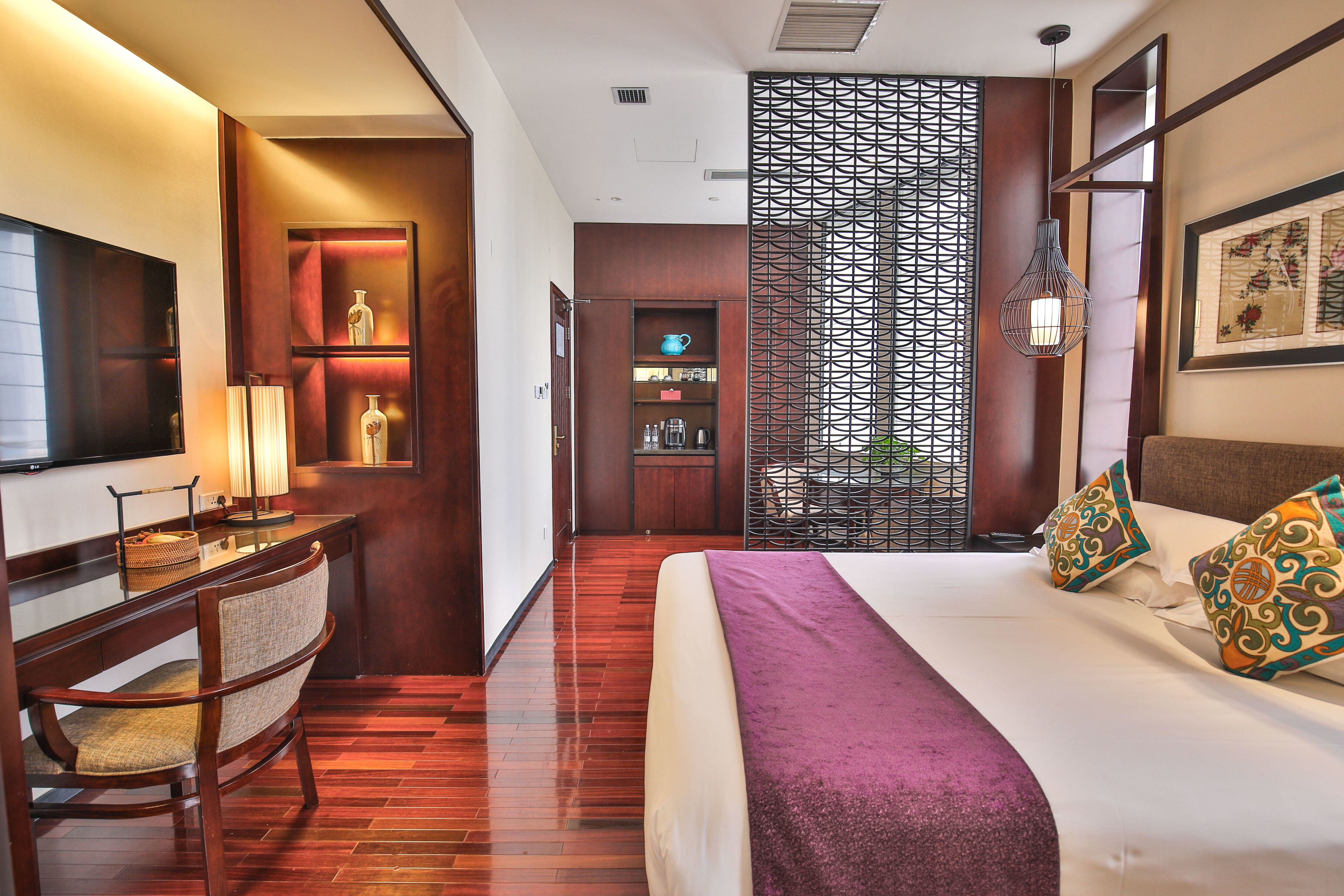 Une chambre d’hôtel comprenant un lit, un bureau avec une chaise, une télévision et un élément de séparation décoratif.