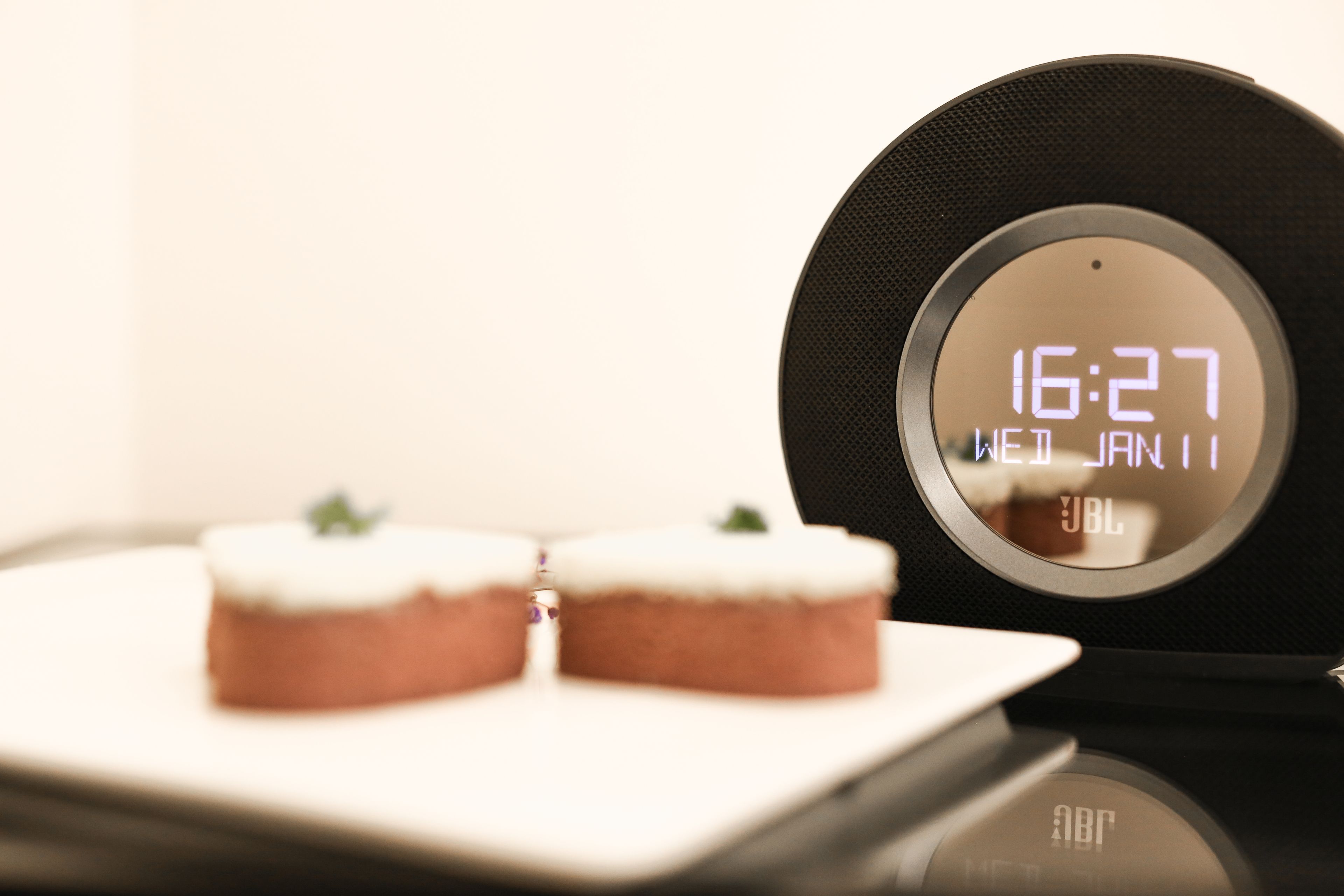 Un reloj digital muestra las 16:27 en un altavoz negro con la marca JBL.