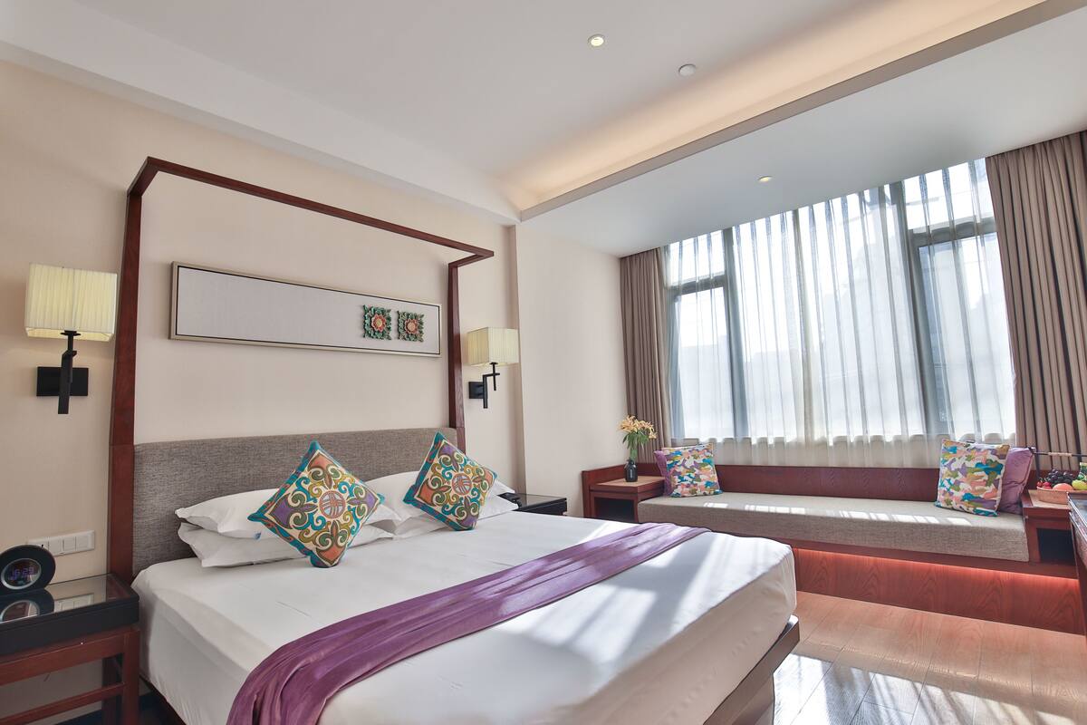 A hotel room with a large bed, a sofa, a desk, and a window with curtains.