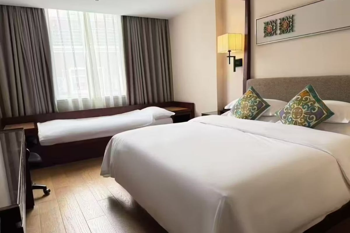 Habitación de hotel con dos camas, un escritorio, una silla, una lámpara y una ventana con cortinas.