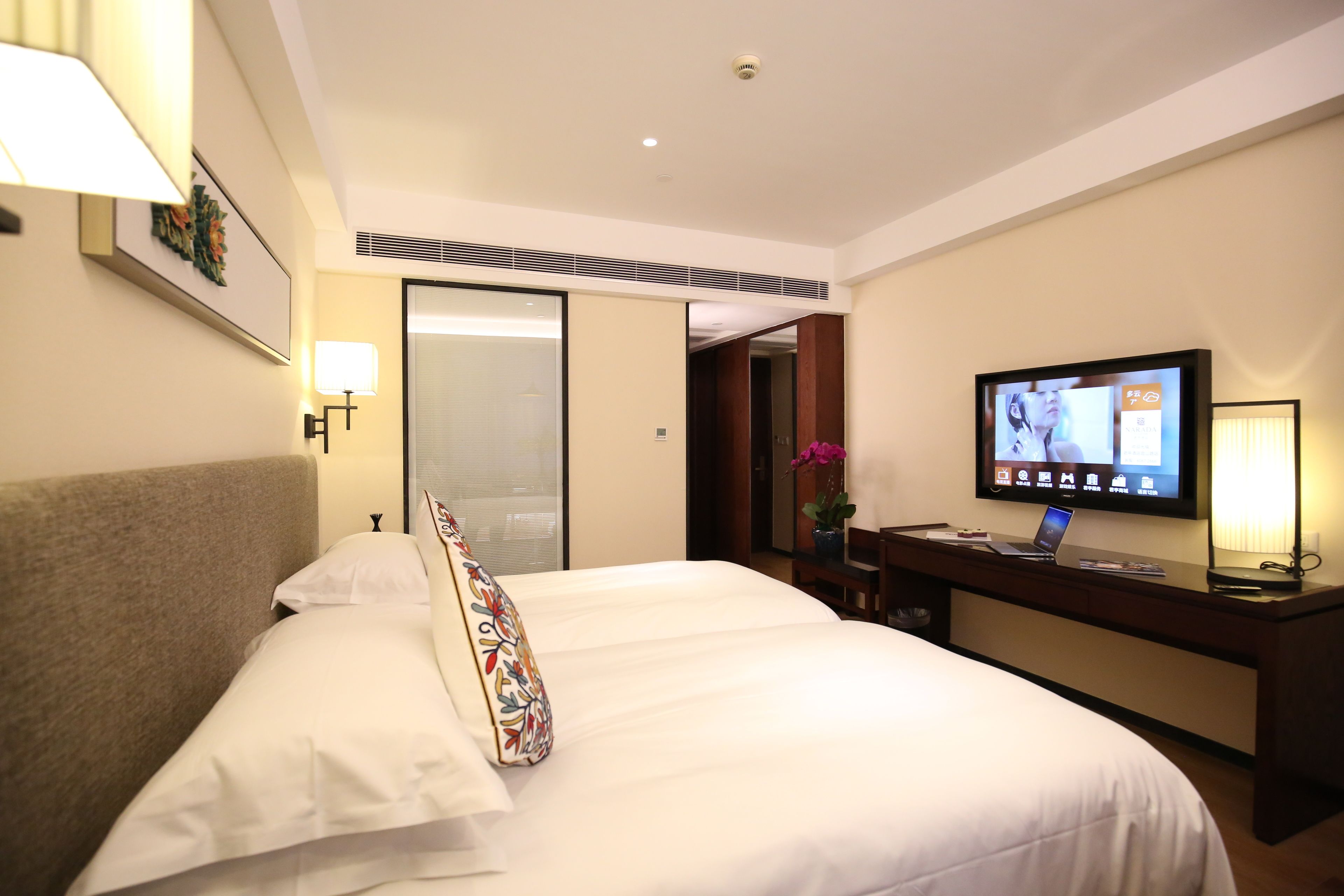 A hotel room with a bed, a desk, a television, and a door leading to another room.