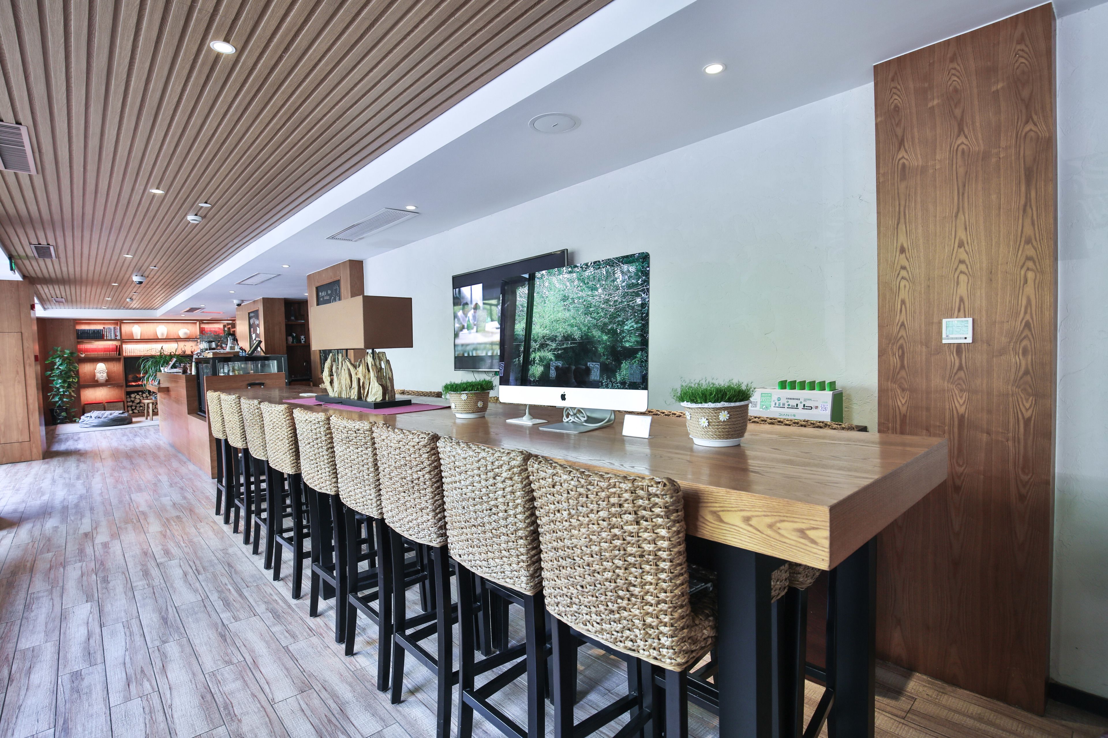 A modern bar area with a wooden ceiling, a long counter with bar stools, and a large window displaying greenery.