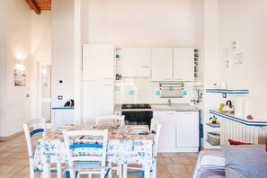 A compact kitchen with white cabinets, a dining table with chairs, and a small refrigerator.