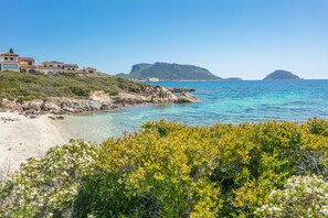 A coastal property with a beach, rocky shoreline, and a view of distant mountains.