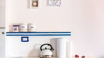 A kitchen with a kettle, two sale jars, a roll of paper towels, and two toy cars on a shelf.