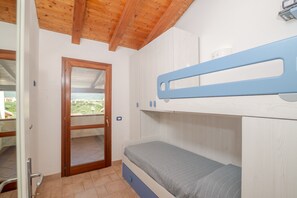 Een slaapkamer met een stapelbed, een houten plafond, een deur naar een balkon en een klein nachtkastje.