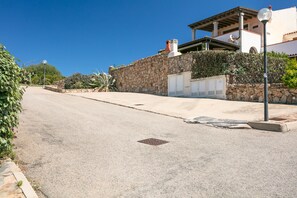A street with a stone wall, a building with a tiled roof, and a street lamp.
