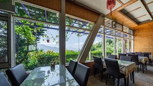 A restaurant with a glass table and chairs, large windows, and a view of greenery and mountains. - Julie's Garden (Ren'ai)