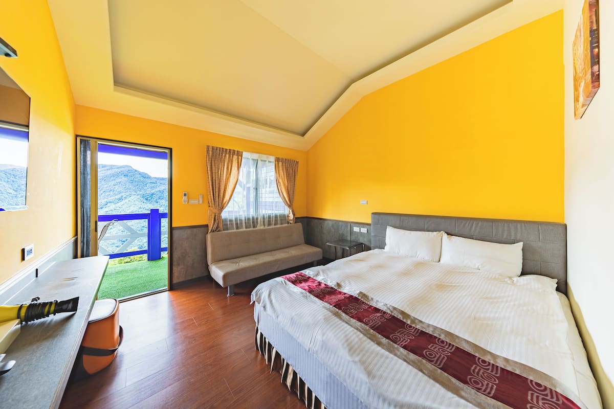 A hotel room with a bed, a sofa, a desk, and a view of the outdoors.