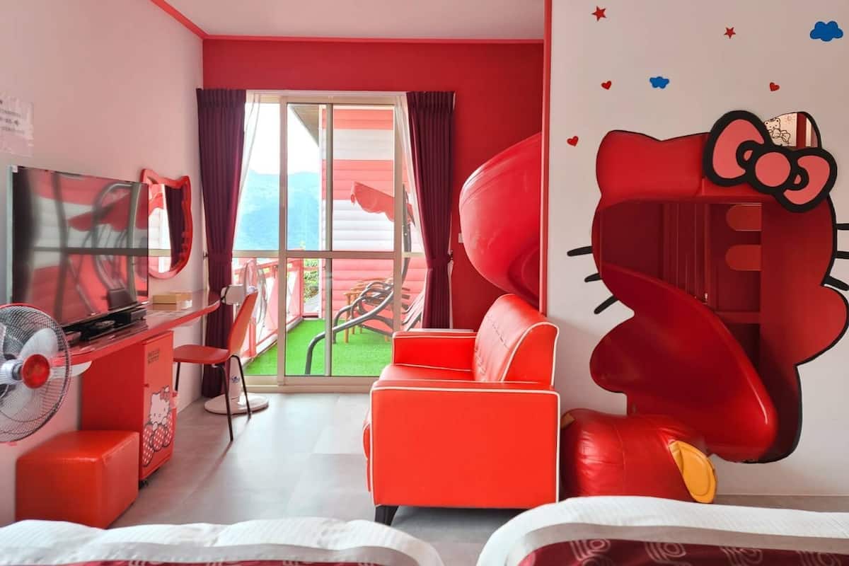 A room with a large window, a red sofa, a TV, and a Hello Kitty mural.