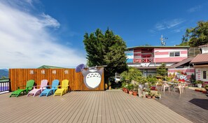 A wooden deck with colorful Adirondack chairs, a large toad sculpture, and potted plants. - Julie's Garden (Ren'ai)
