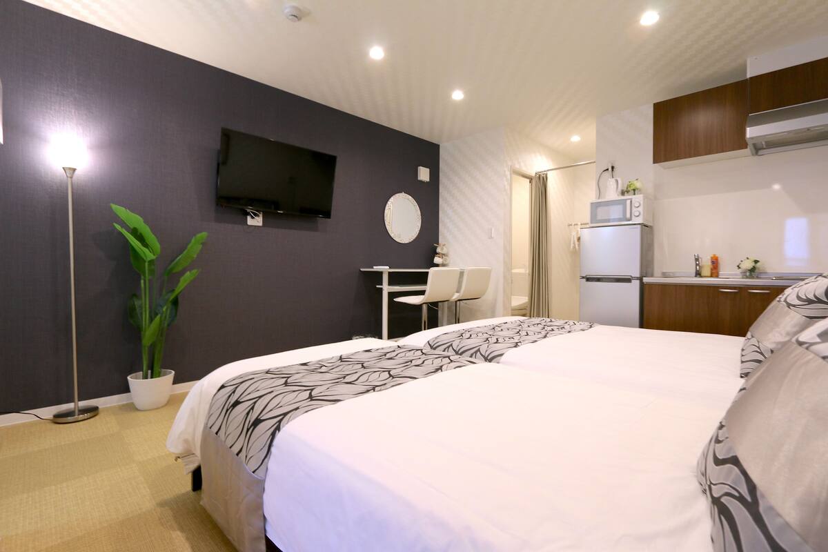 A modern hotel room with a large bed, a desk, a chair, a flat-screen TV, a microwave, and a potted plant.