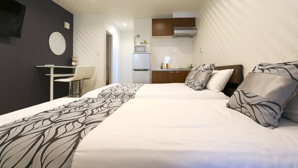 Ett hotellrum med två sängar, ett skrivbord, en stol, en TV och ett litet kök.