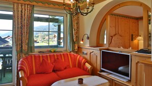 A cozy room with a sofa, TV, and a view of a mountainous landscape. - No. 9 Fewo Talblick - Gästehaus Braito (Grän)
