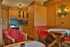 L’intérieur d’un chalet en bois comprend une cuisine, deux fauteuils rembourrés, une table et un luminaire fixé au mur.