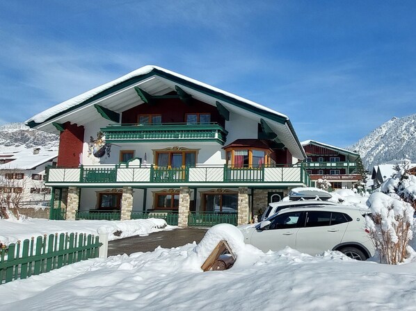 Un hotel grande y de varios pisos con fachada nevada, balcones y montañas al fondo.