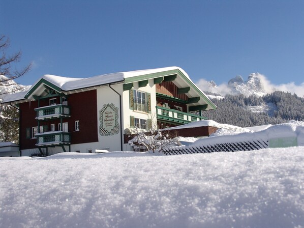 Un edificio cubierto de nieve con balcones, un letrero y un paisaje montañoso de fondo.