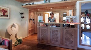 Zona de recepción con mostrador de madera, una persona de pie detrás y una puerta que da a otra habitación.