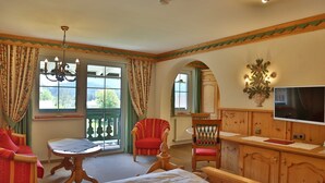 Una habitación con cama, dos sillas, una mesa, televisor y ventana con cortinas.