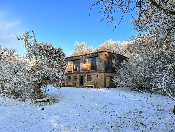 Una casa de dos pisos con un balcón, rodeada de árboles cubiertos de nieve.