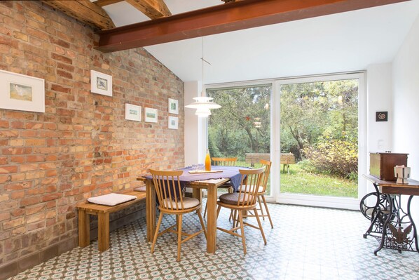 Un comedor con pared de ladrillo, sillas de madera, una mesa y vistas a través de un ventanal.