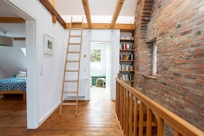 Dormitorio tipo loft con escalera de madera, estantería y vistas a través de una puerta abierta.