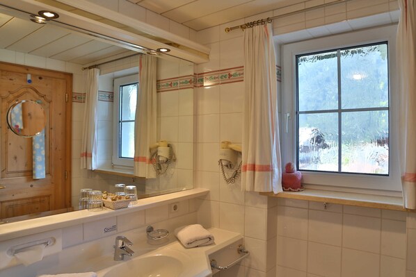 A bathroom with a large mirror, a window with curtains, a sink, and a bathtub.