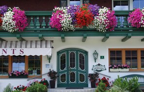 A building with a green door, multiple flower boxes with various flowers, and a sign indicating 'Apartments Komfortzimmer.'