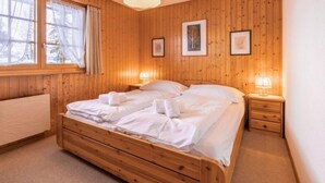 Una habitación acogedora de madera con una cama grande, dos mesitas de noche con lámparas y cuadros enmarcados en la pared.