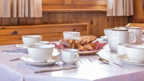 Desayuno con cruasanes, tazas de café y una mesa preparada para cuatro personas.