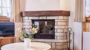 Una sala de estar acogedora con una chimenea de piedra, un televisor y una mesa redonda con un jarrón de flores.