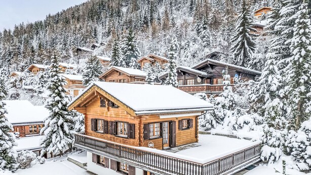 Una cabaña de madera con balcón, rodeada de árboles nevados y un paisaje montañoso.