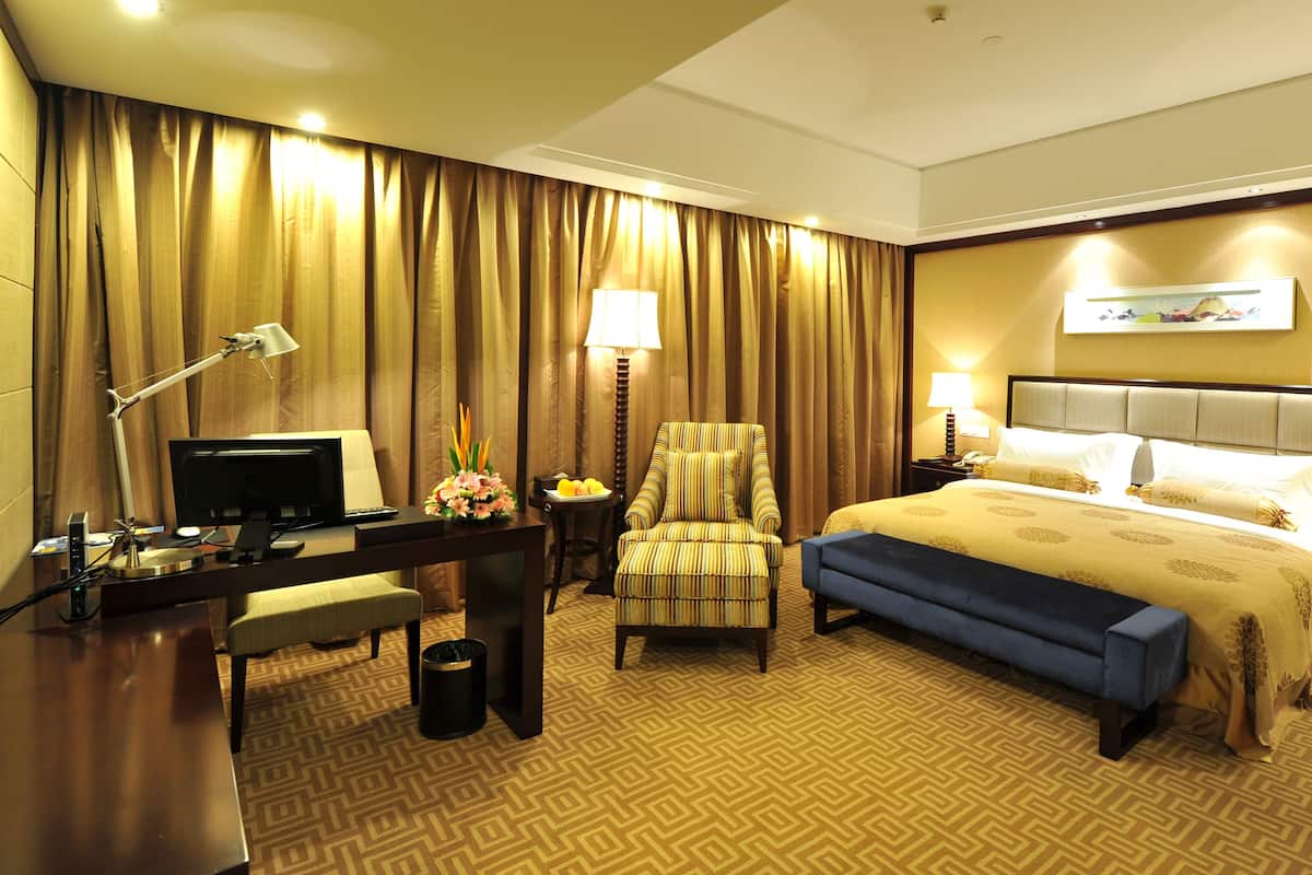Een hotelkamer met een groot bed, een bureau met een computer, een stoel en een kleine tafel met een lamp.