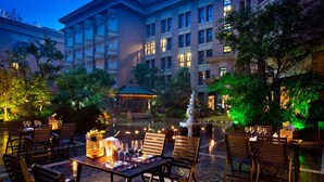 An outdoor dining area with tables and chairs, a fountain, and a building in the background. - Nanjing Greenland Yuhao Hot Spring Hotel (Nanjing)