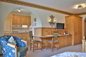 Une pièce comprenant une table à manger, deux chaises, un canapé, des meubles en bois, un téléviseur et une plante décorative.