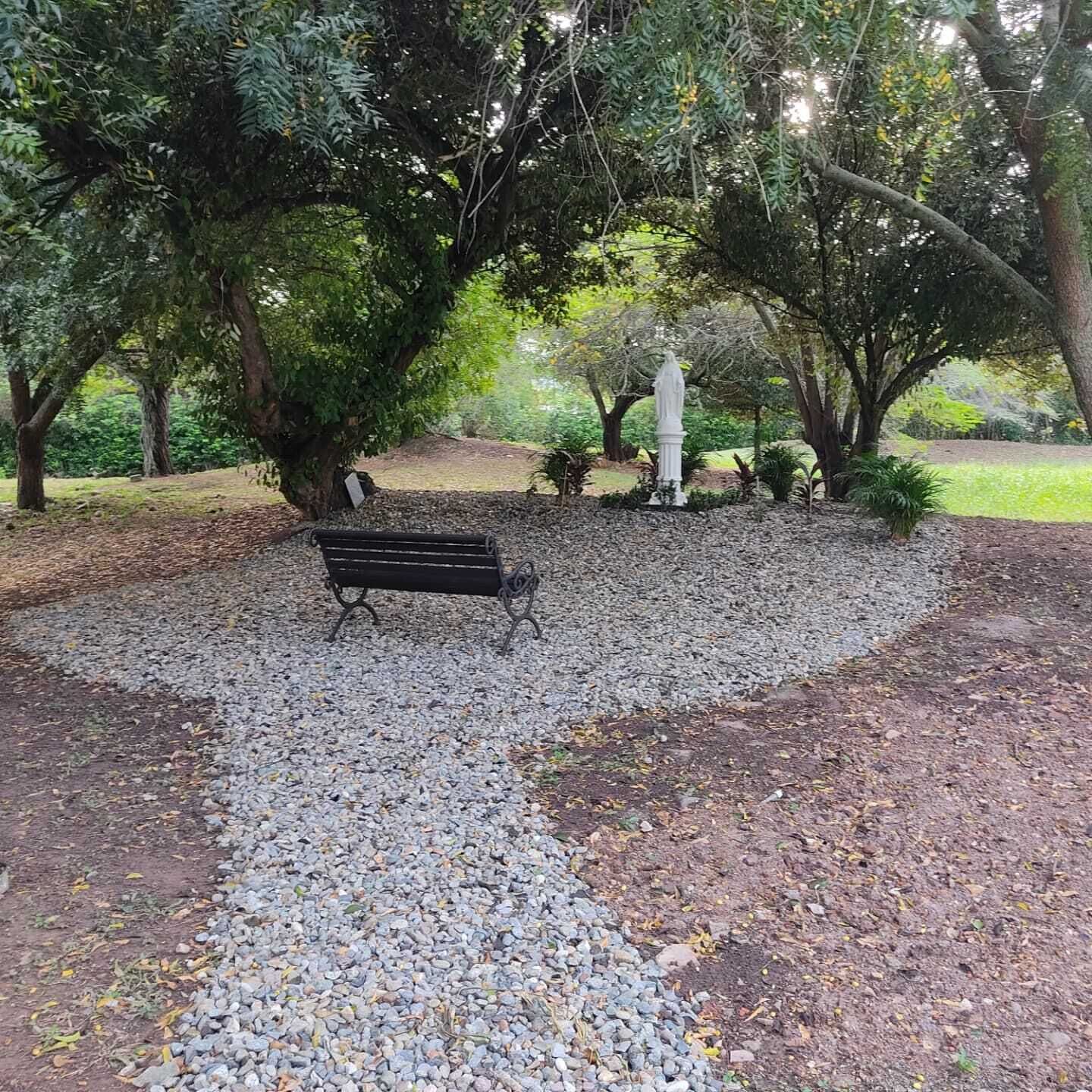 Un parque con un sendero de grava, una banca y una estatua.